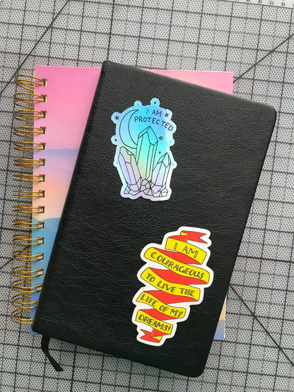 "I Am Protected" holographic sticker + "I Am Courageous" matte sticker on journal cover