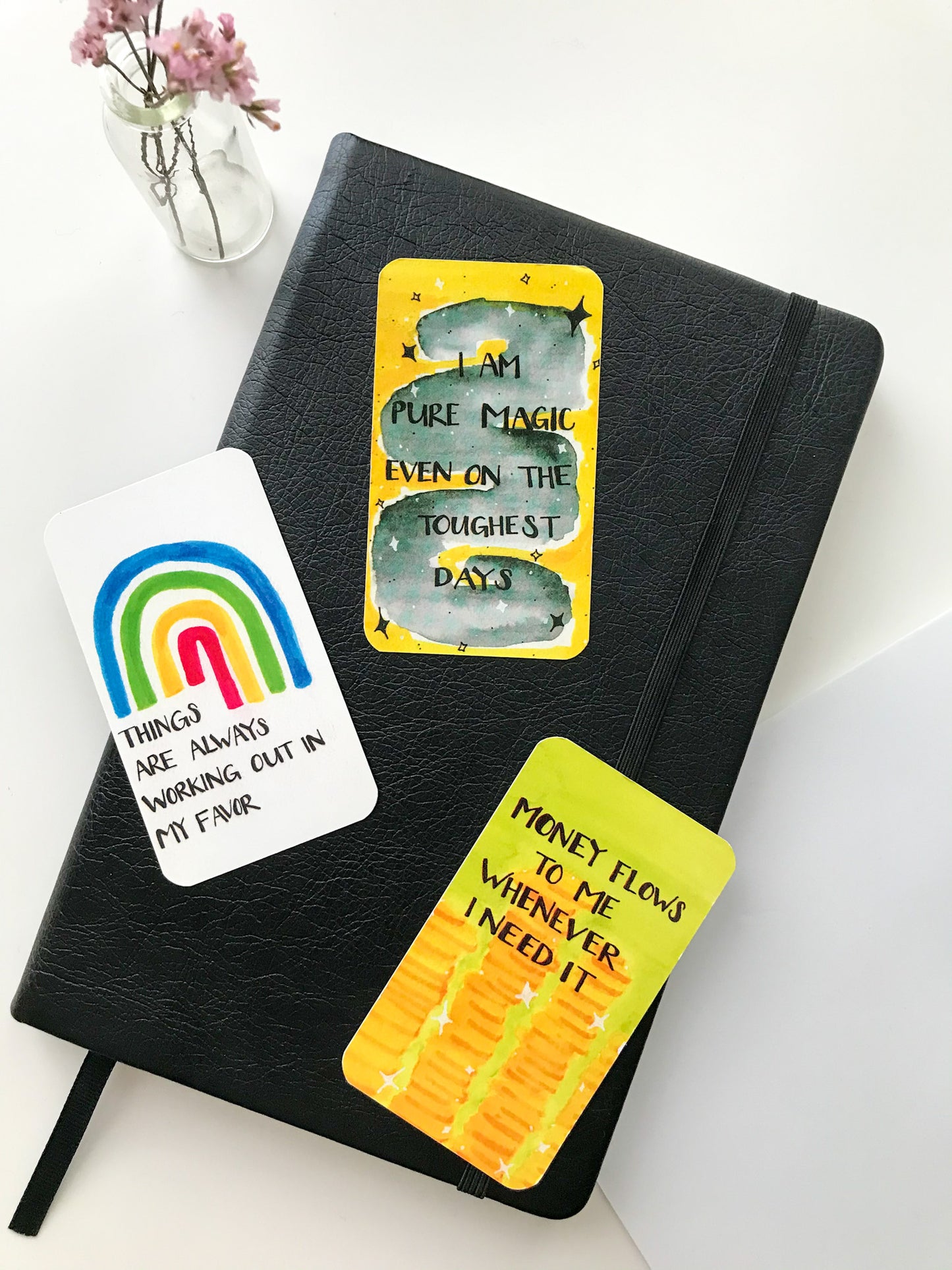 #MOOD Magnet Set of three (3) on top of a black journal. From left to right, magnets read: Things are always working out in my favor; I am pure magic even on my toughest days; Money flows to me whenever I need it.